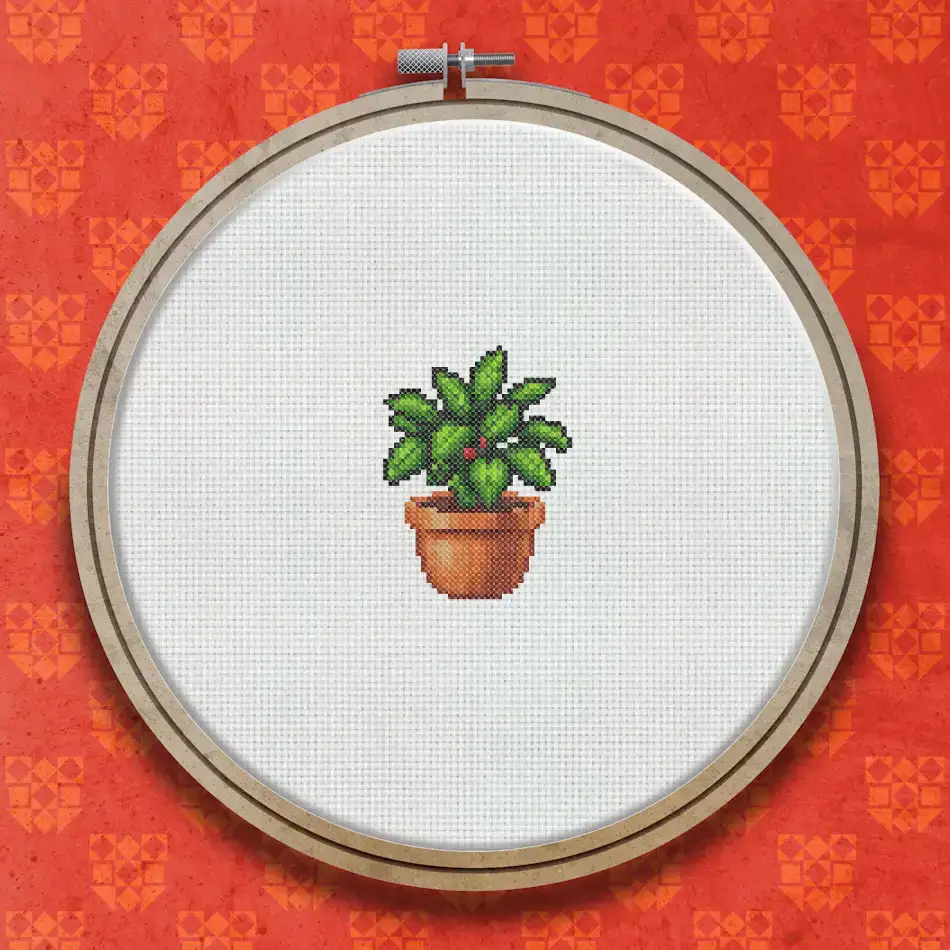 Cross stitch design of a small leafy green plant in a terracotta pot with rounded foliage and earthy brown tones.