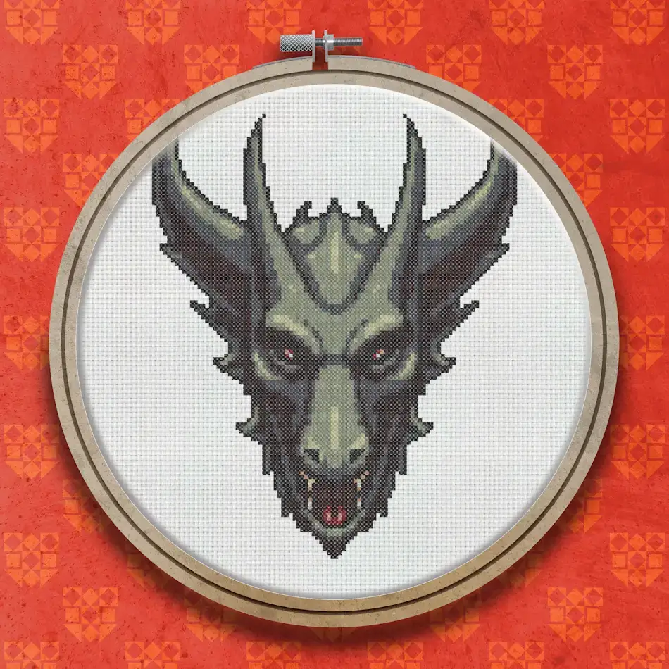 Cross stitch design of a gargoyle face with curved horns, green-grey stone-textured skin, deep-set eyes and a slightly open mouth showing teeth, on a dark background.