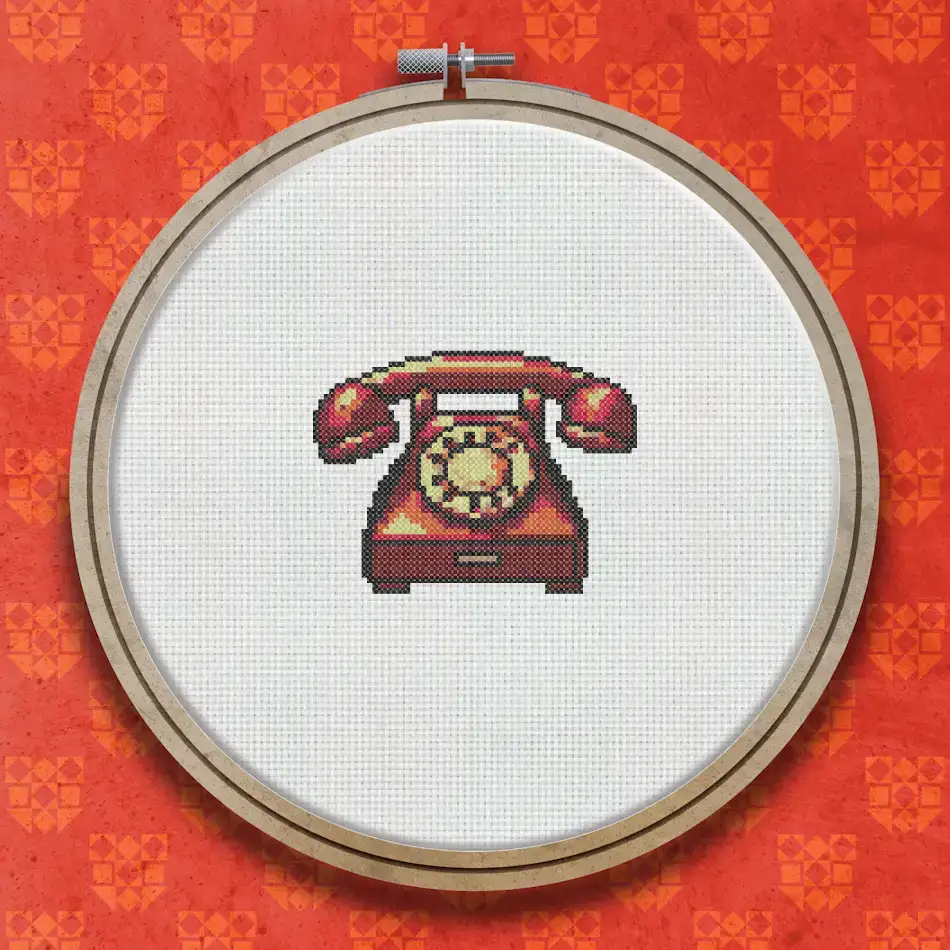 Cross stitch design of a red vintage rotary telephone with a circular dial, curved handset, and cream base details on a white background.