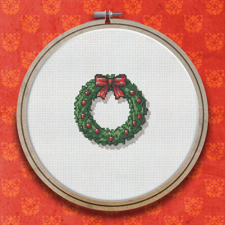 Cross stitch wreath with dark green foliage, red berries, and a large red ribbon bow with a gold bell at the top.