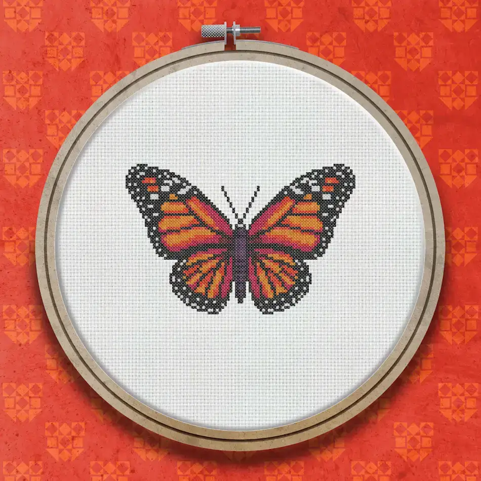 Finished cross stitch of a monarch butterfly with bright orange wings, bold black outlines, and white spots along the wing edges.