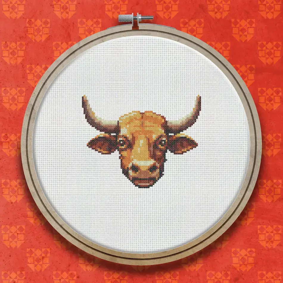 Cross stitch pattern of a brown bull's head facing forward with curved horns, warm golden-brown tones and a detailed muzzle on a white background.