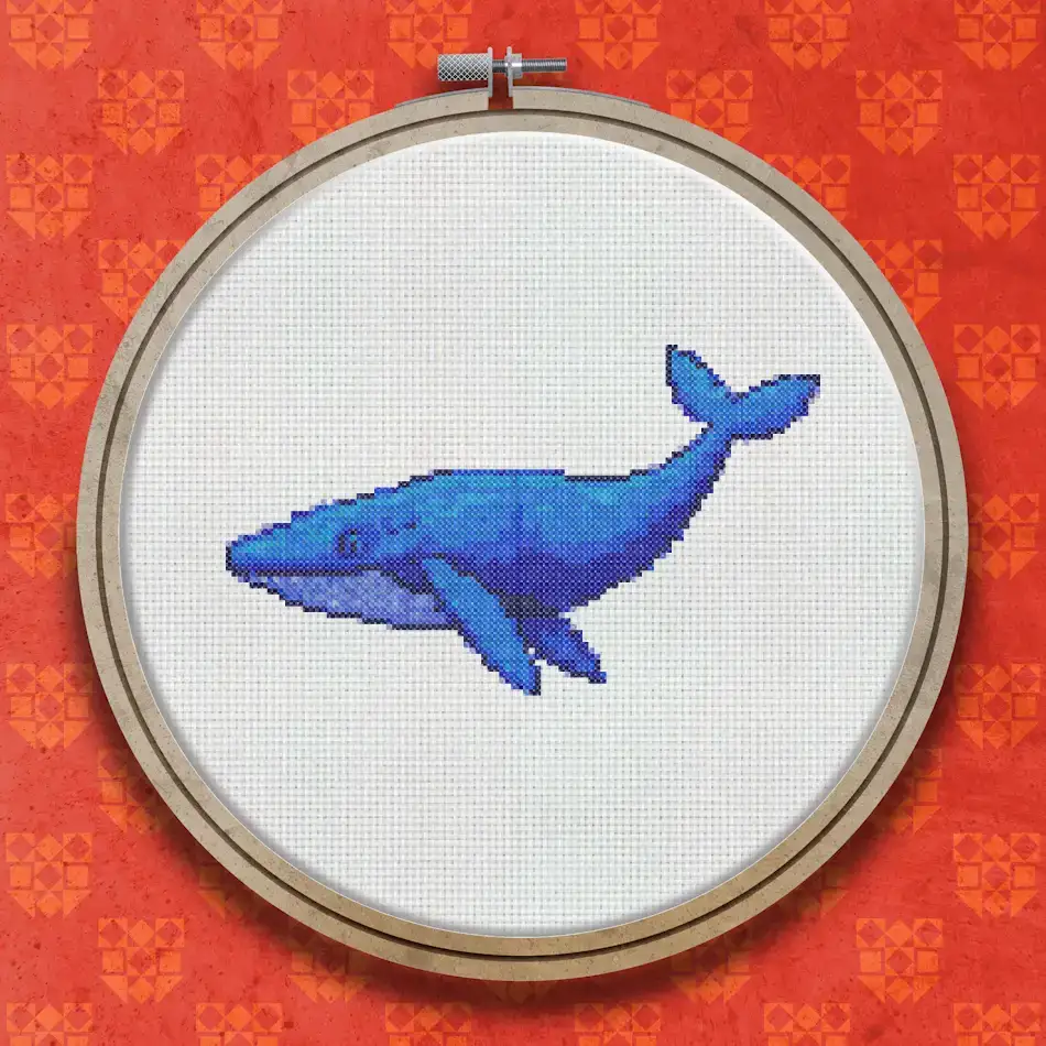 Cross stitch pattern of a blue whale shown in profile, stitched in shades of blue with a pale underside, facing left against a white background.