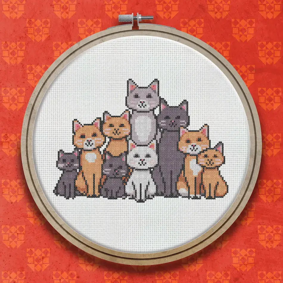 Cross stitch design of seven cats grouped together, including ginger, grey, dark grey, brown and white cats, sitting closely as a group