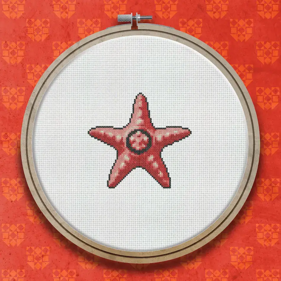 Cross stitch pattern of a red starfish with five arms spread outward, worked in warm red and pink tones on a white background.