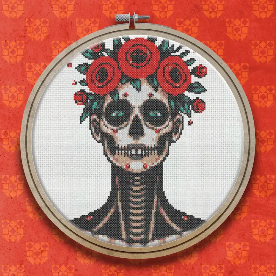 Cross stitch design of a Day of the Dead skeleton with a floral rose crown, wearing a black outfit with red and white details on a white background.