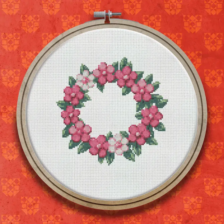 Circular cross stitch wreath with pink five-petal flowers, small white blossoms, and green leaves arranged in a full ring.