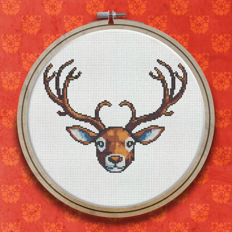 Cross stitch portrait of a reindeer face with large branching antlers, rendered in warm brown, tan and cream tones on a white background.