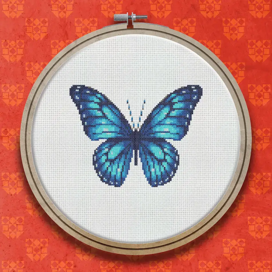Cross stitch pattern of a blue butterfly with open wings, featuring deep sapphire and electric blue shades with black detailing on the wing edges.