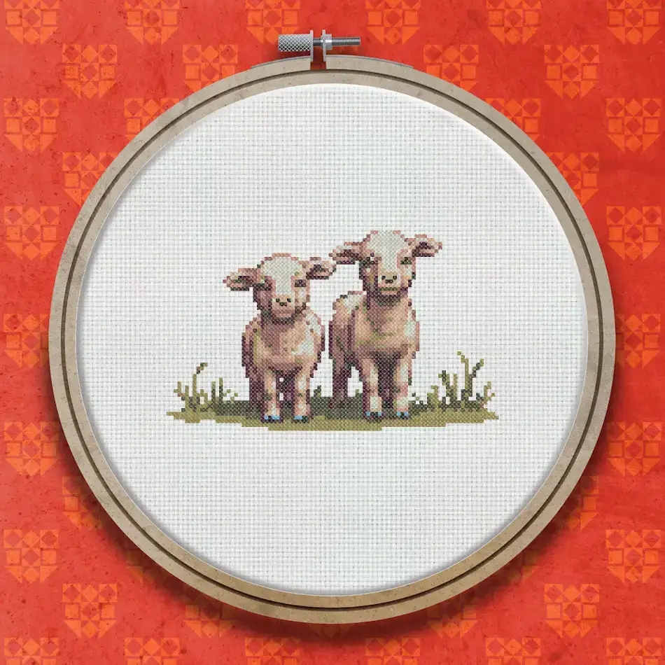 Two white fluffy lambs with pink faces standing together on green grass, stitched in a warm and characterful cross stitch style.