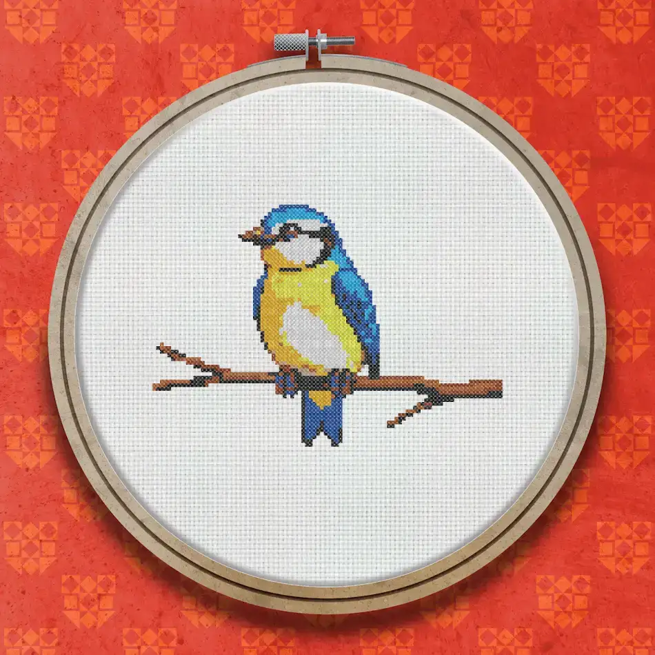 Cross stitch design of a blue tit with blue and yellow feathers perched on a brown branch against a white background.