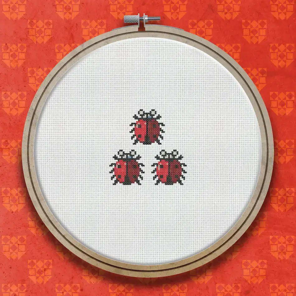 Three red ladybirds with black spots arranged in a small group, stitched in cross stitch on a white fabric background.