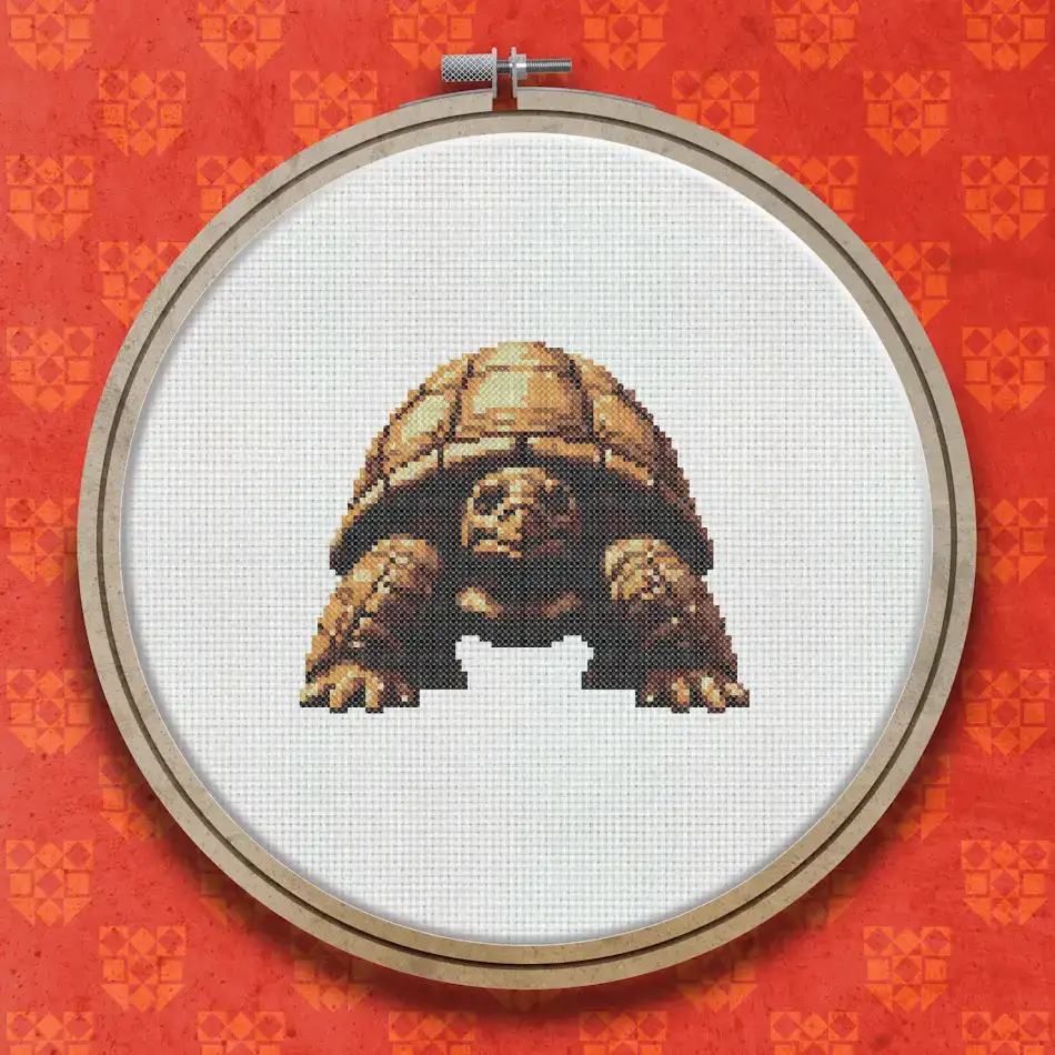Cross stitch pattern of a giant tortoise viewed head-on, showing a large domed brown shell with darker shading and a textured, weathered face.