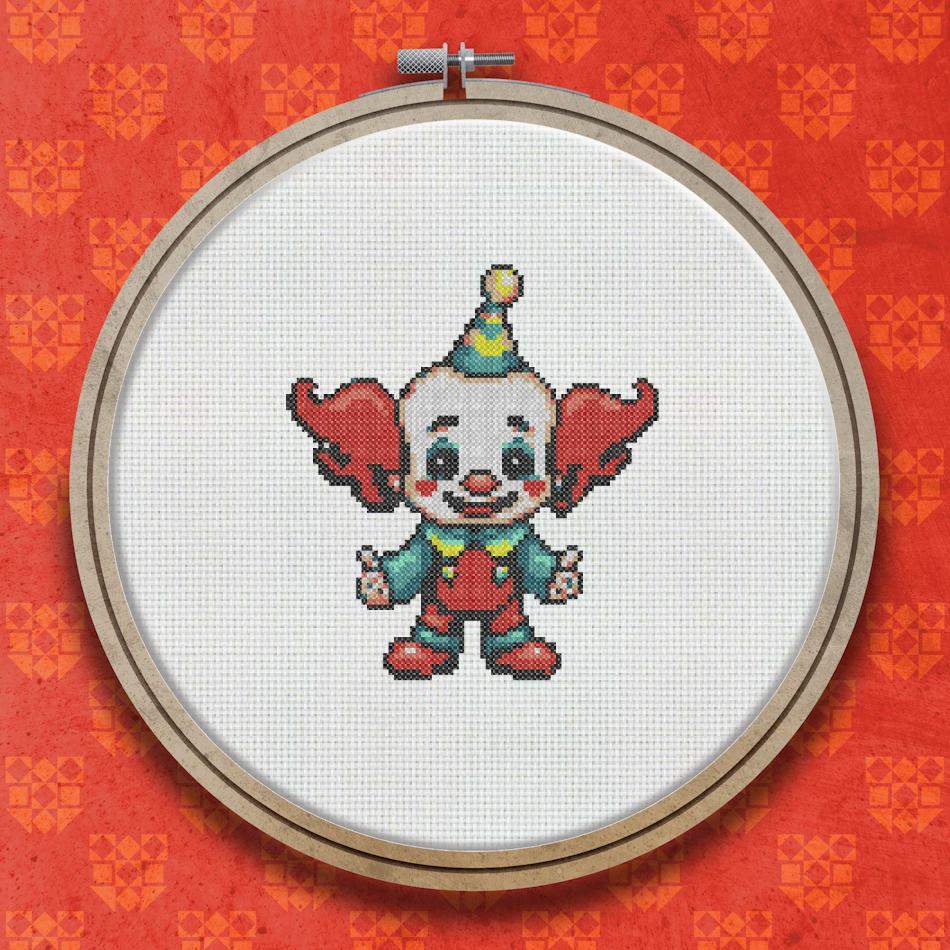 A small cross stitch clown wearing a yellow and green pointed hat, red pompoms, a red and white striped outfit, and oversized red shoes, with a round smiling face.
