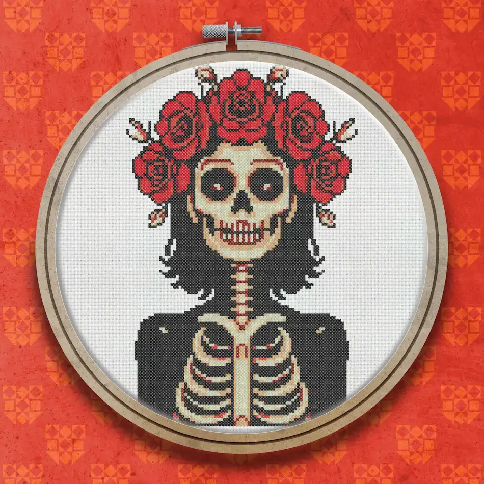 Cross stitch pattern of a Day of the Dead sugar skull with a floral rose crown, dark hair, and a visible ribcage, in red, black and cream tones.