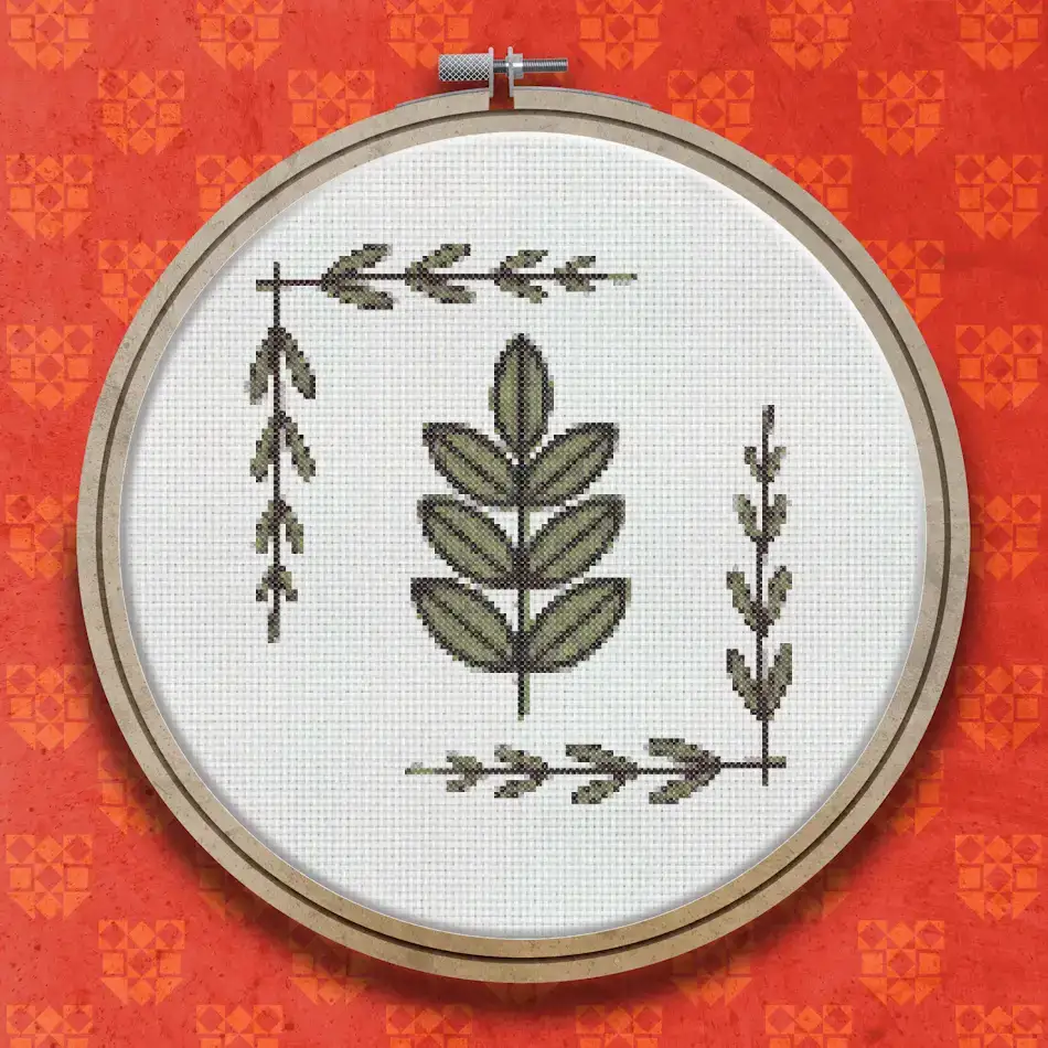 Cross stitch design showing a central leafy green sprig with oval leaves, flanked by two vertical trailing branches with small pointed leaves, on a cream background.