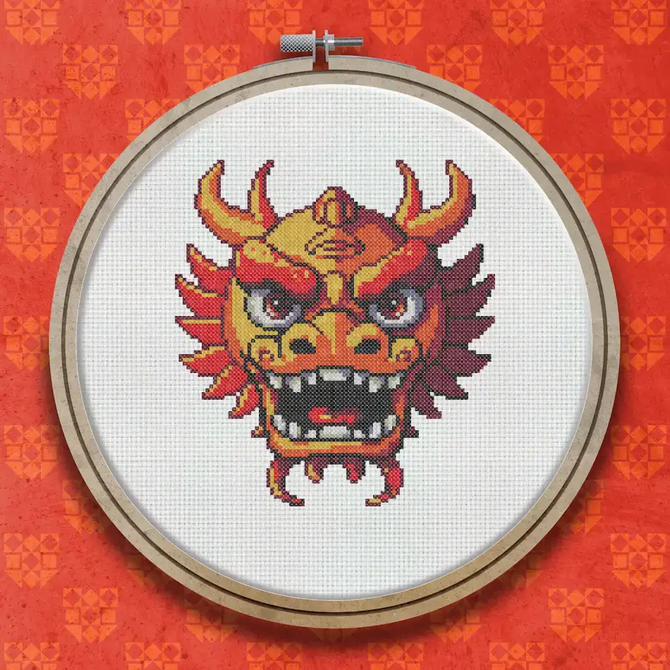 Cross stitch pattern of a red and orange Chinese festival dragon mask with golden horns, fierce expression and decorative detailing.