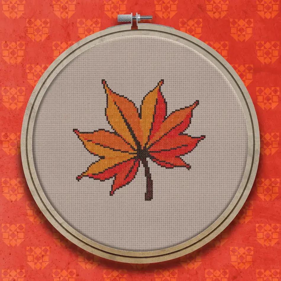 A cross stitch design of a single large autumn leaf in shades of red, orange and brown with a pointed lobed shape.