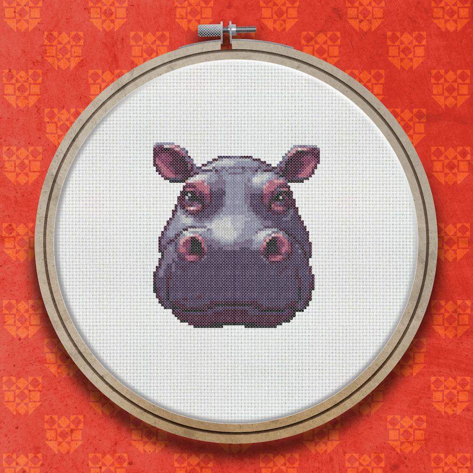 Cross stitch pattern of a hippopotamus face shown front-on, with muted purple and grey tones, small rounded ears, and a broad muzzle.