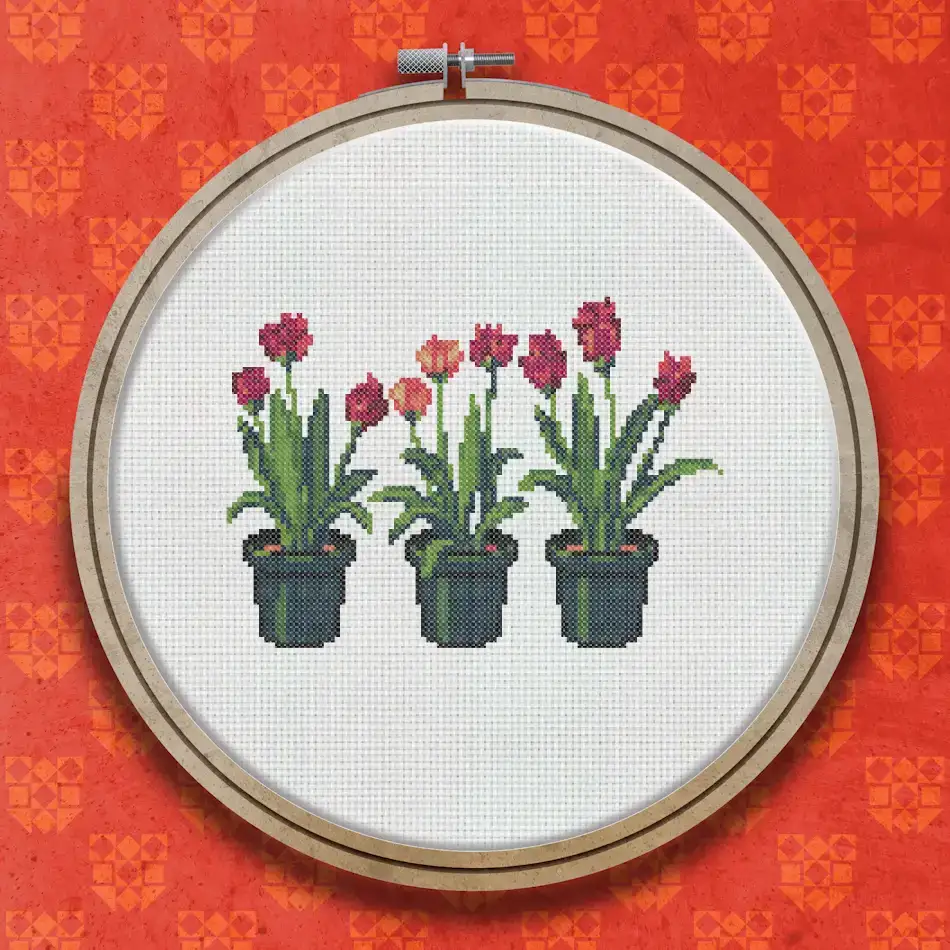 Cross stitch design showing three pink tulips with green leaves growing in dark soil in green plant pots, arranged side by side.