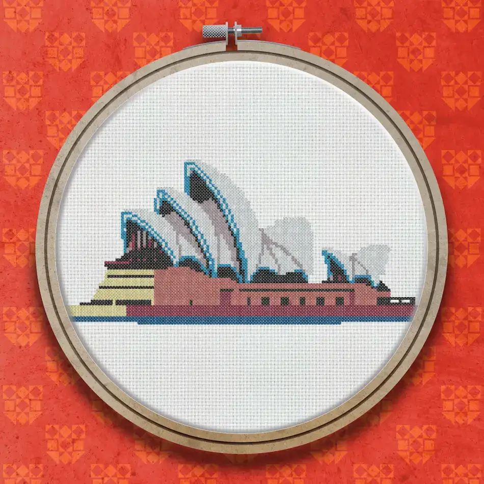 Cross stitch pattern of the Sydney Opera House showing white shell-shaped roof structures on a blue sky background above a red-brown harbour wall.