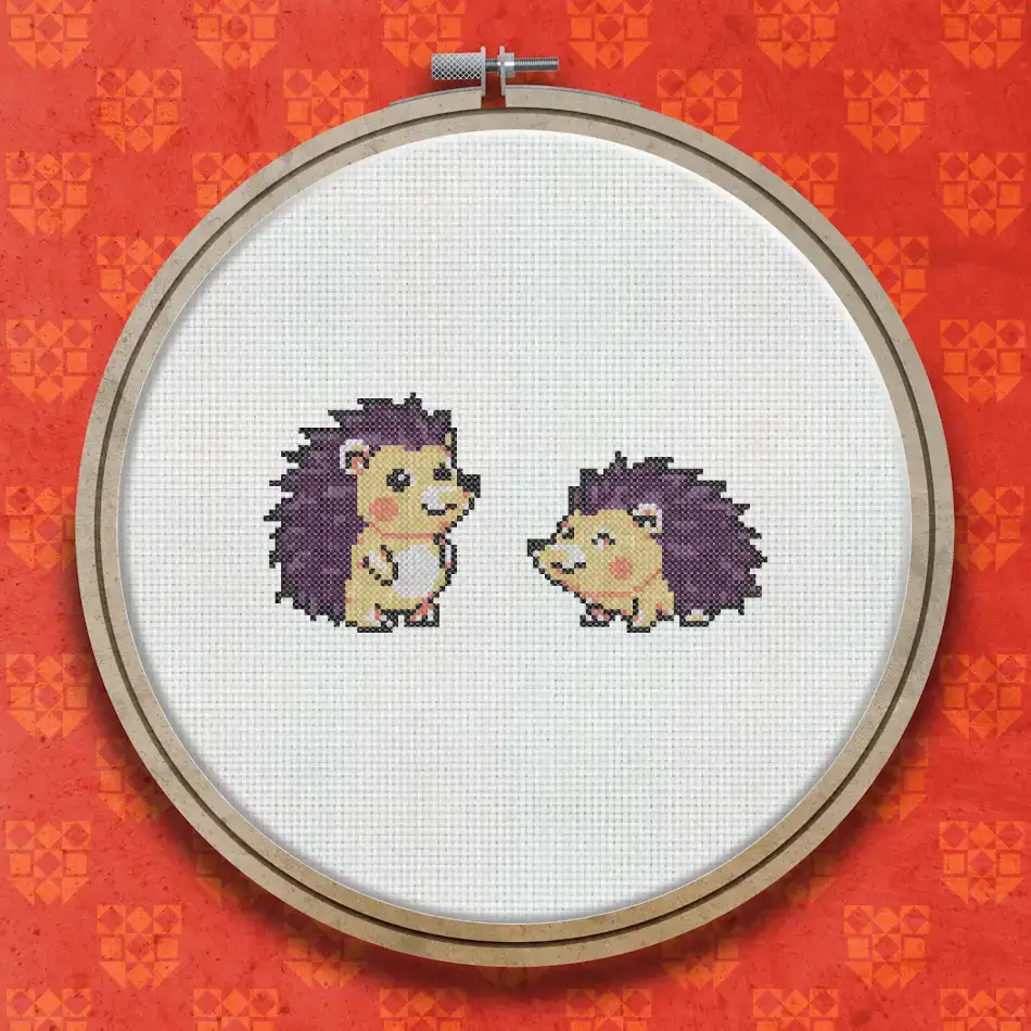 Two small cross stitch hedgehogs standing side by side, shown in brown and cream tones on a white background.