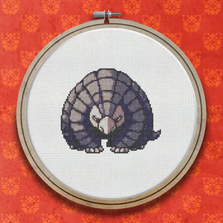 Cross stitch pattern of a pangolin viewed from the front, showing its rounded scaly body in shades of grey and brown, with small clawed feet visible beneath.