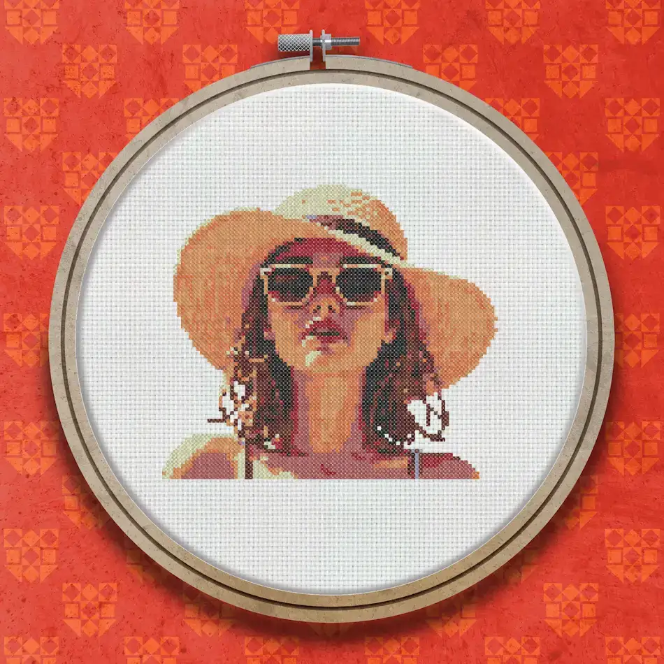 Cross stitch portrait of a young woman wearing a wide-brimmed straw hat and sunglasses in warm summer sunlight.