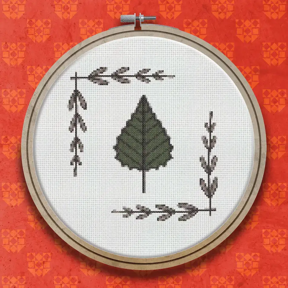 Cross stitch pattern of a single large green birch leaf centred on a white background, with small decorative twig and leaf sprigs in each corner
