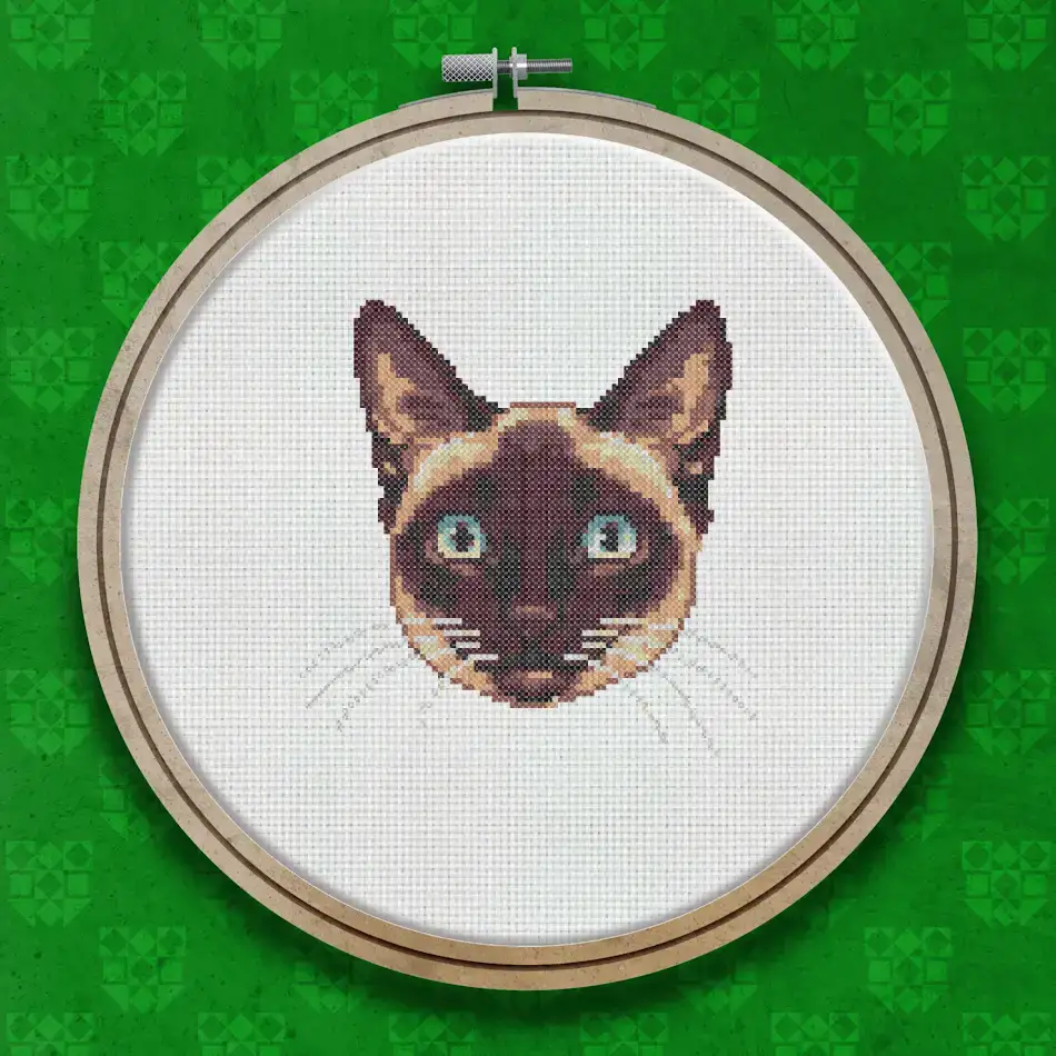 Cross stitch portrait of a Siamese cat face with blue eyes, dark seal-point markings on ears and face, and a cream-coloured coat.