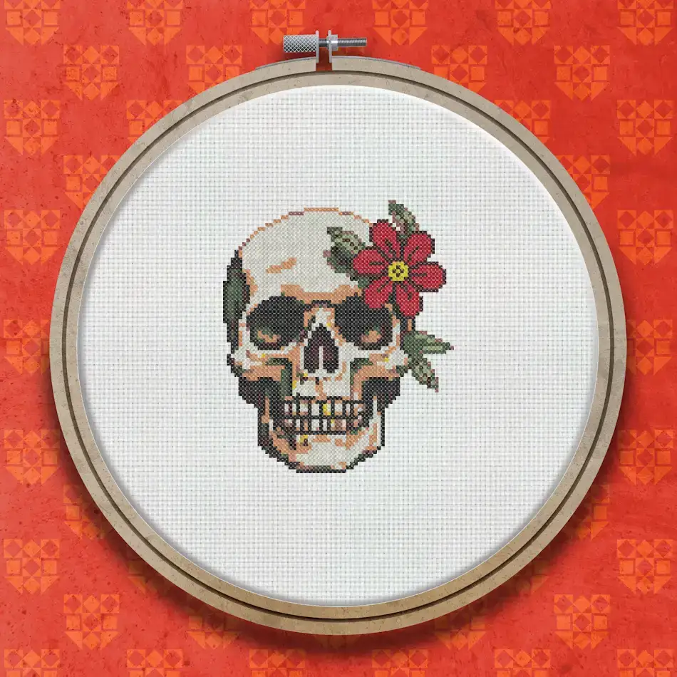 Cross stitch design of a human skull facing forward with a red flower on top, decorated in warm cream, brown and colourful tones.