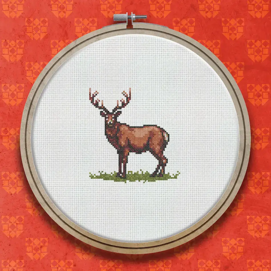 Cross stitch design of a brown stag with antlers standing on green grass, shown in a naturalistic side-facing pose.